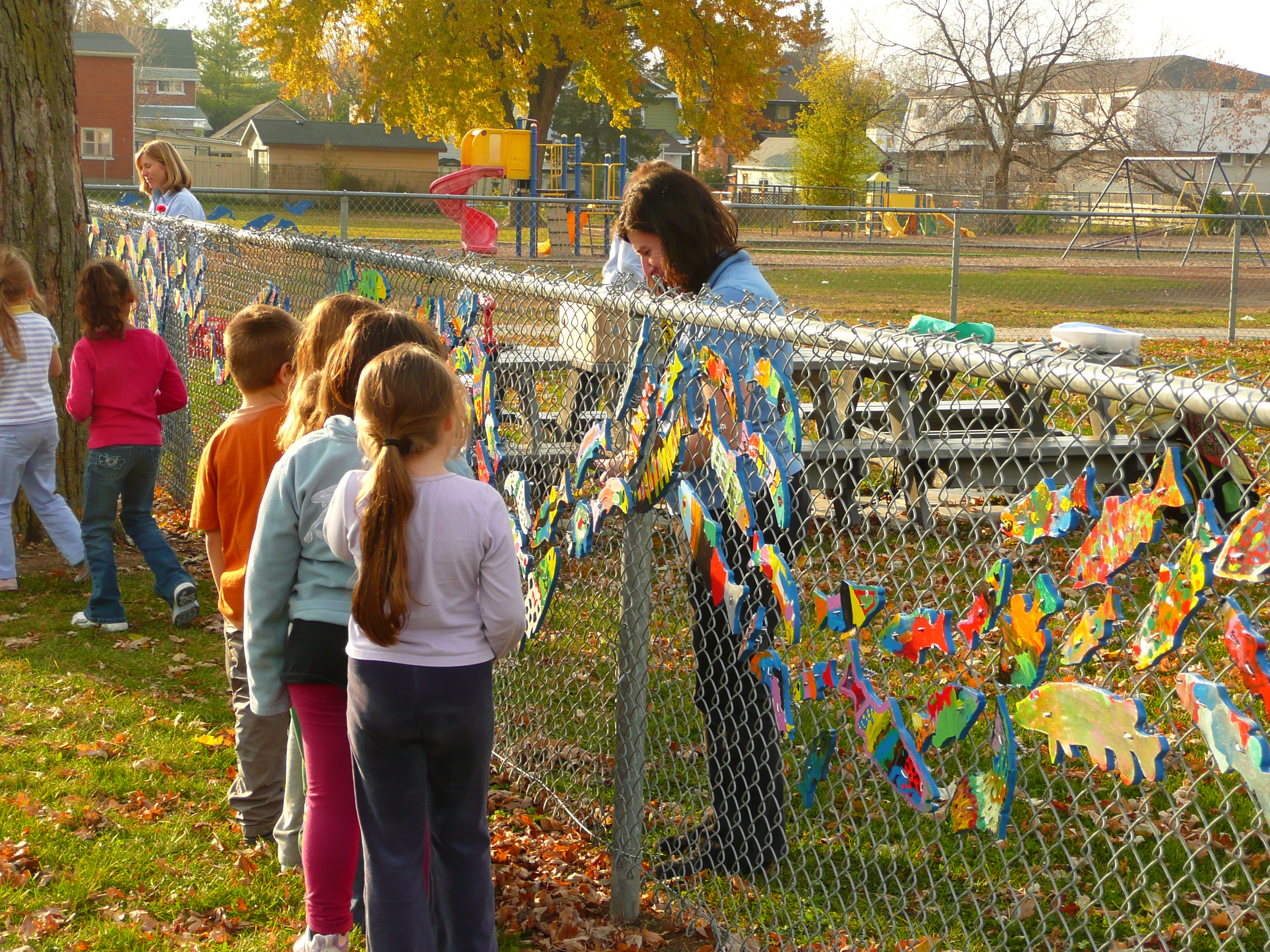 Children looking at painted fish on a fence infront of a school